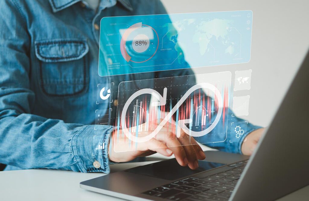 A person in a denim shirt uses a laptop with glowing digital overlays. The graphics feature a large infinity loop, an 88% progress ring, a world map, and colorful data charts, representing continuous workflows and real-time analytics.